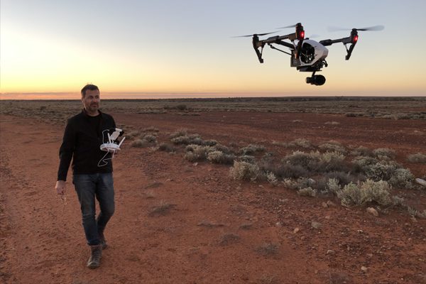 Drone operator flying a drone in the outback at sunset