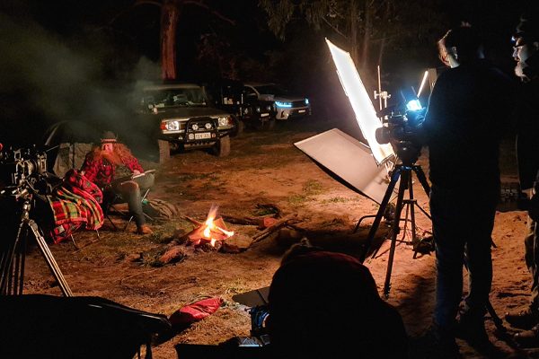 Film crew night shoot with lighting rig and campfire